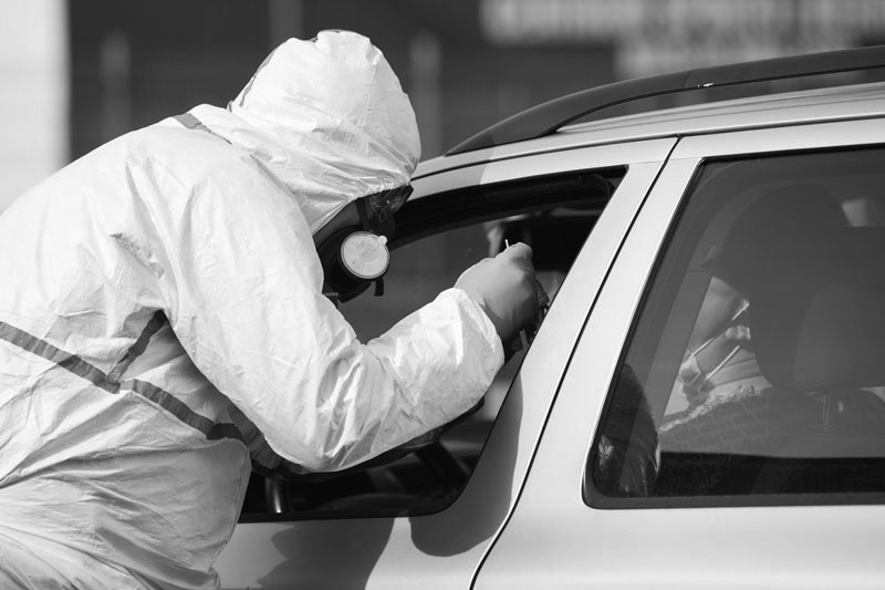 Person with full PPE conducts covid test from car