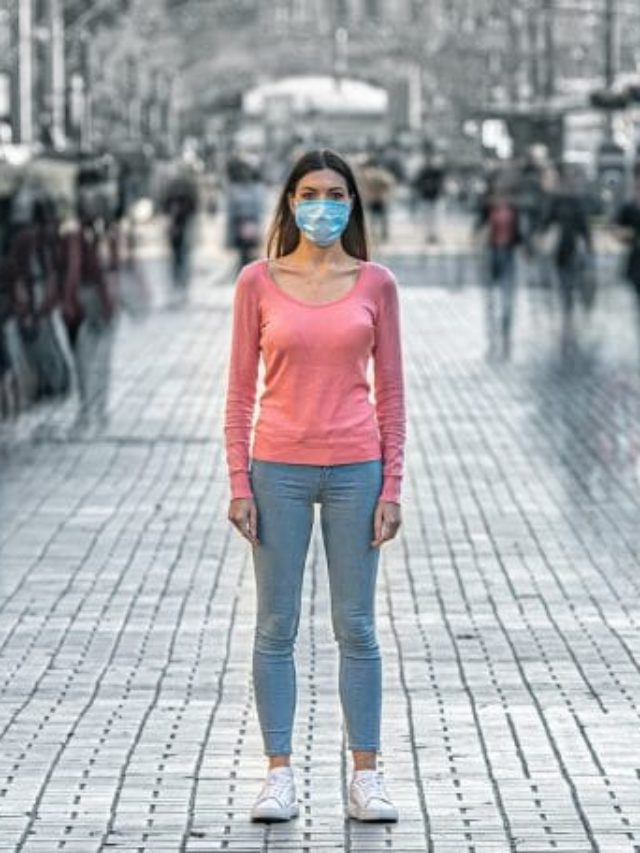 IMAGE: A woman is standing alone wearing a mask