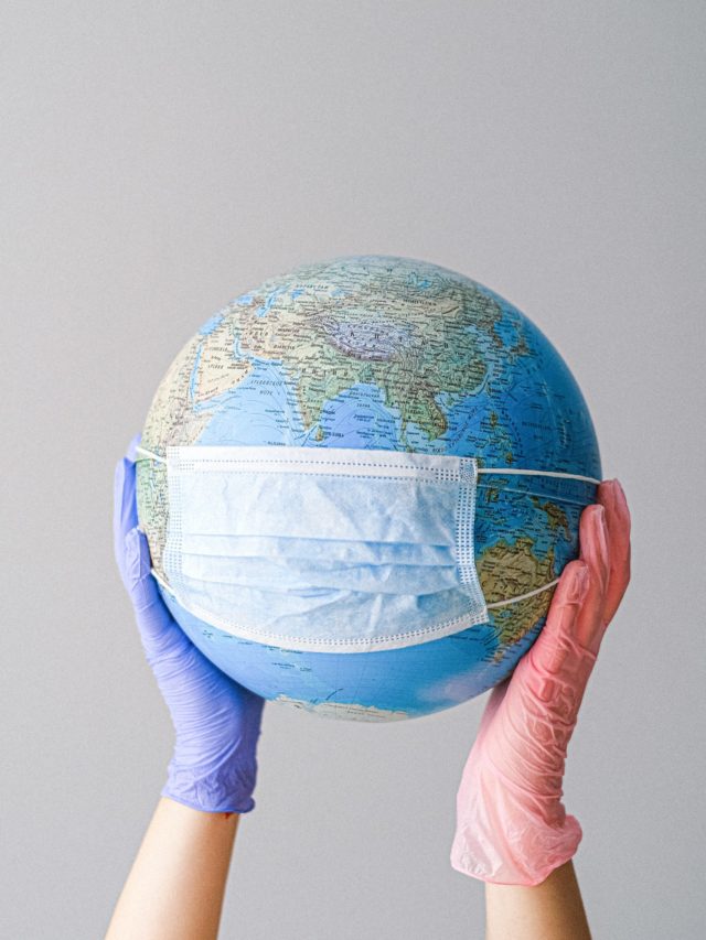 IMAGE: Two hands holding a globe up that is wearing a mask